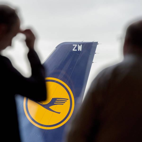 Zwei Männer blicken auf dem Flughafen durch ein Fenster auf eine abgestellte Lufthansa-Maschine.