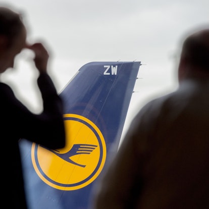 Zwei Männer blicken auf dem Flughafen durch ein Fenster auf eine abgestellte Lufthansa-Maschine.