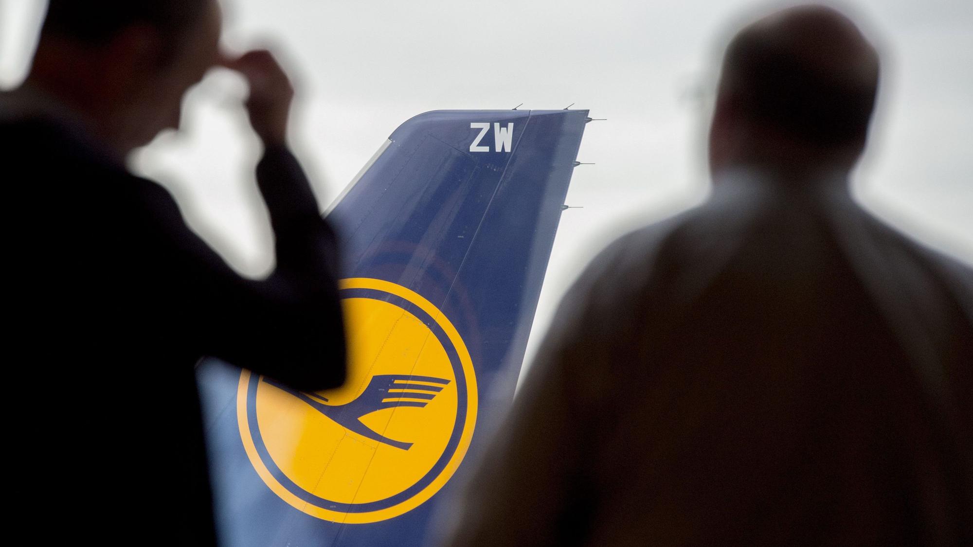 Zwei Männer blicken auf dem Flughafen durch ein Fenster auf eine abgestellte Lufthansa-Maschine.