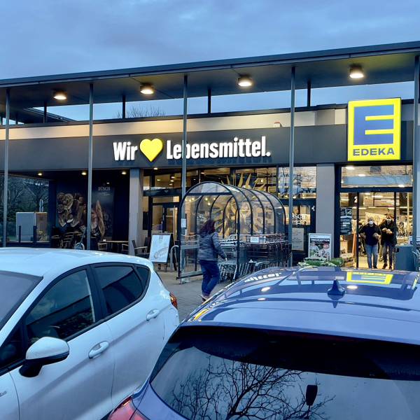 Der Eingang einer Edeka-Filiale mit parkenden Autos im Vordergrund.
