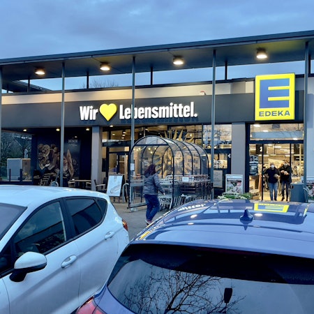 Der Eingang einer Edeka-Filiale mit parkenden Autos im Vordergrund.