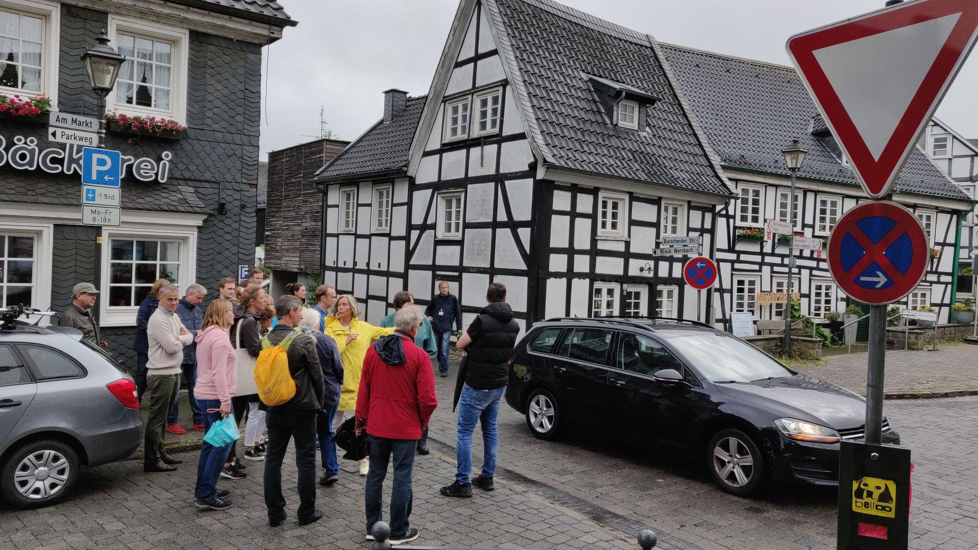 Eine Bürgergruppe steht am Witzheldener Marktplatz an der Einmündung der Burscheider Straße zwischen Fachwerkhäusern.