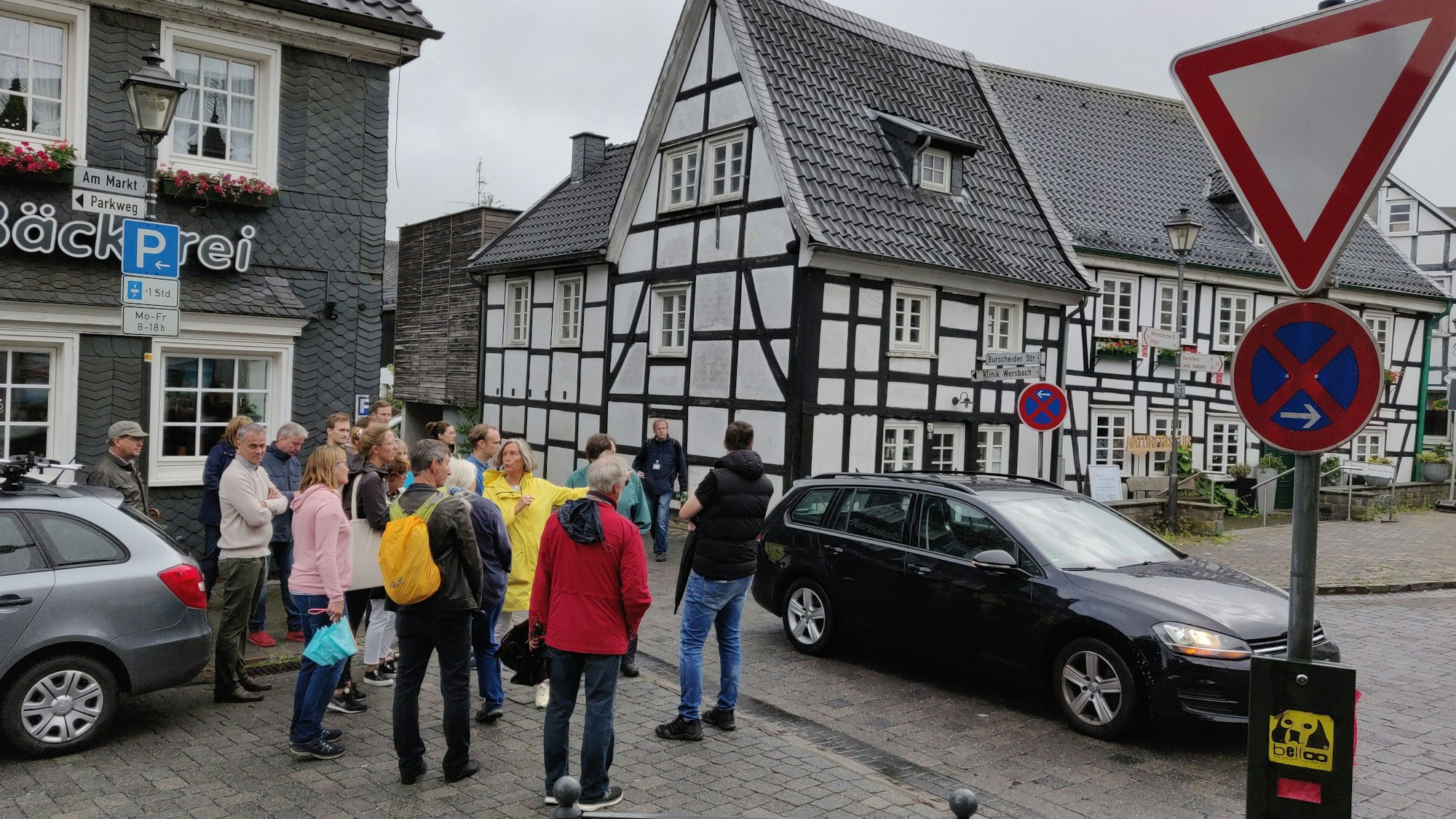 Eine Bürgergruppe steht am Witzheldener Marktplatz an der Einmündung der Burscheider Straße zwischen Fachwerkhäusern.