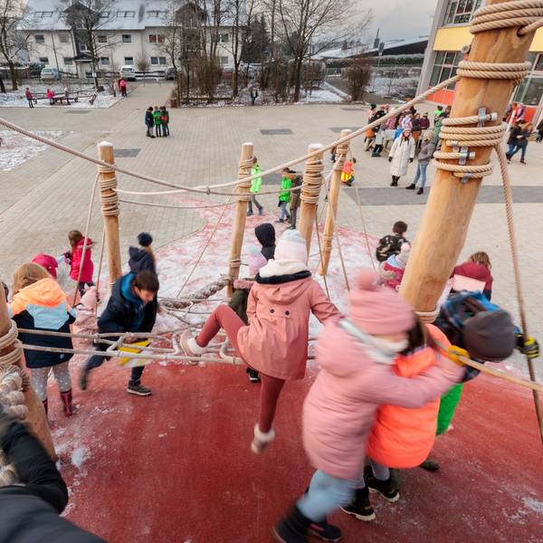 Zahlreiche Kinder klettern auf einem großen Klettergerüst, das auf einem Schulhof steht.