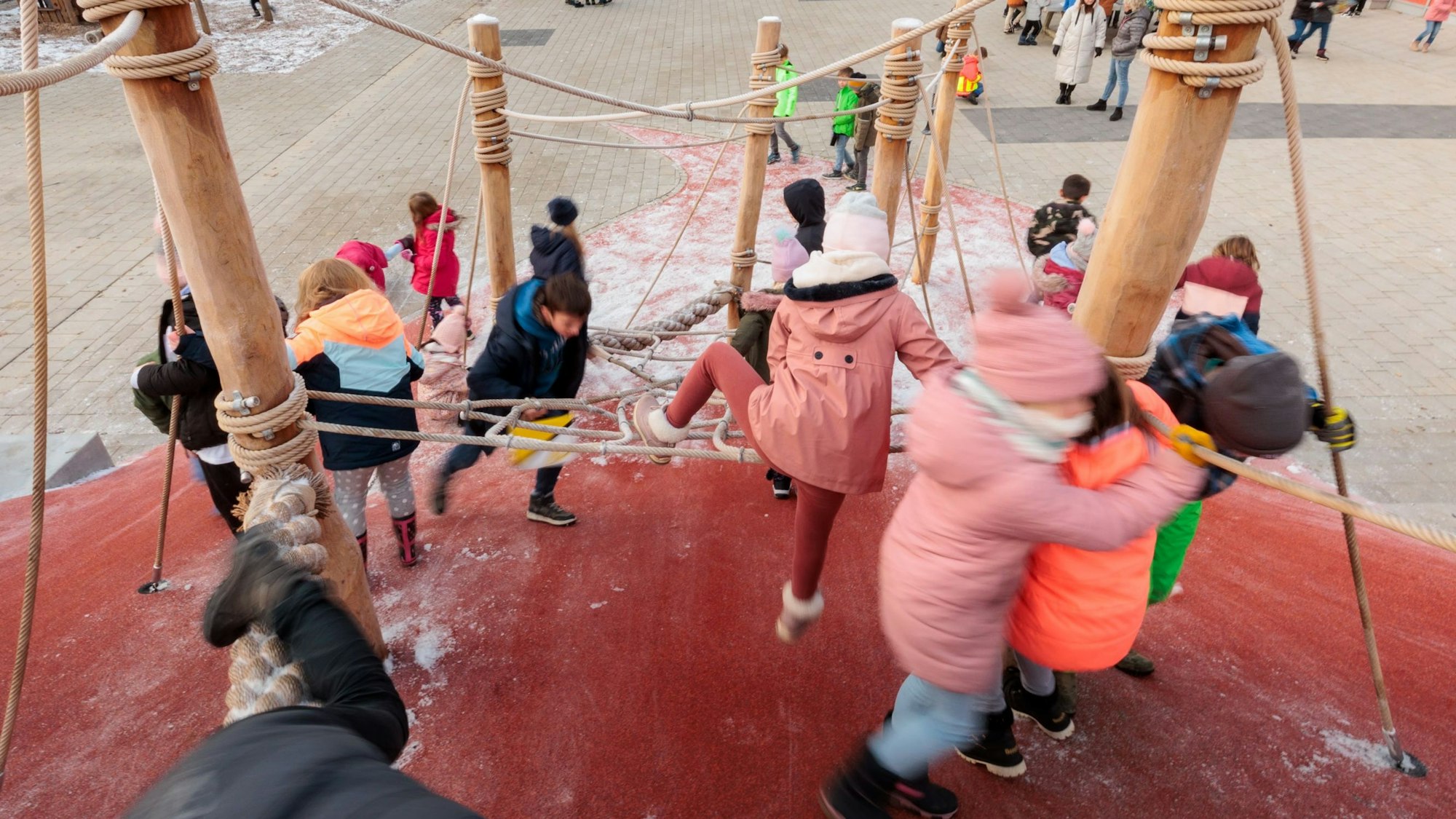 Zahlreiche Kinder klettern auf einem großen Klettergerüst, das auf einem Schulhof steht.