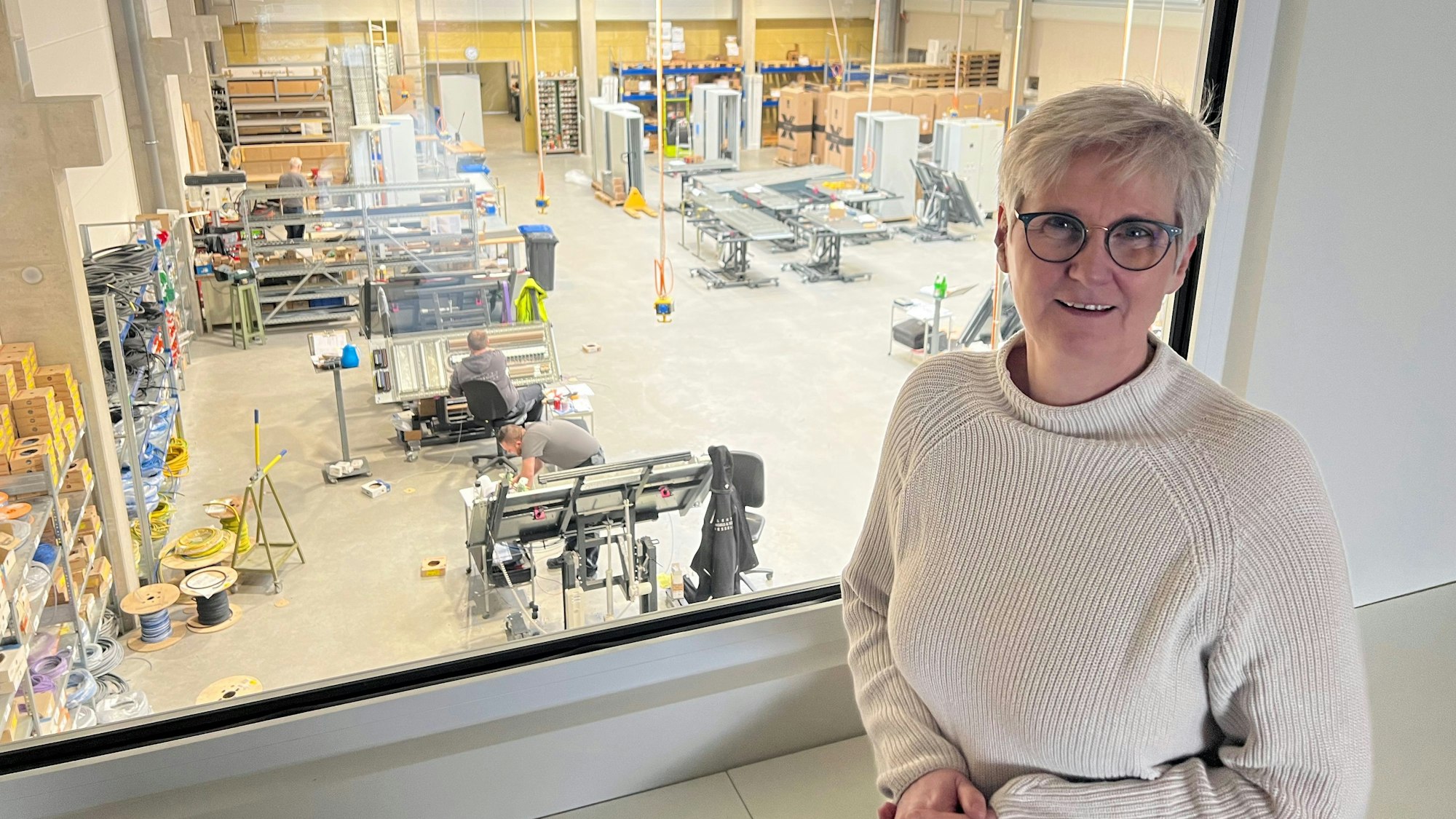 Martina Engels-Bremer steht im Besprechungsraum des Unternehmens. Von dort aus blickt sie in die Werkshalle.