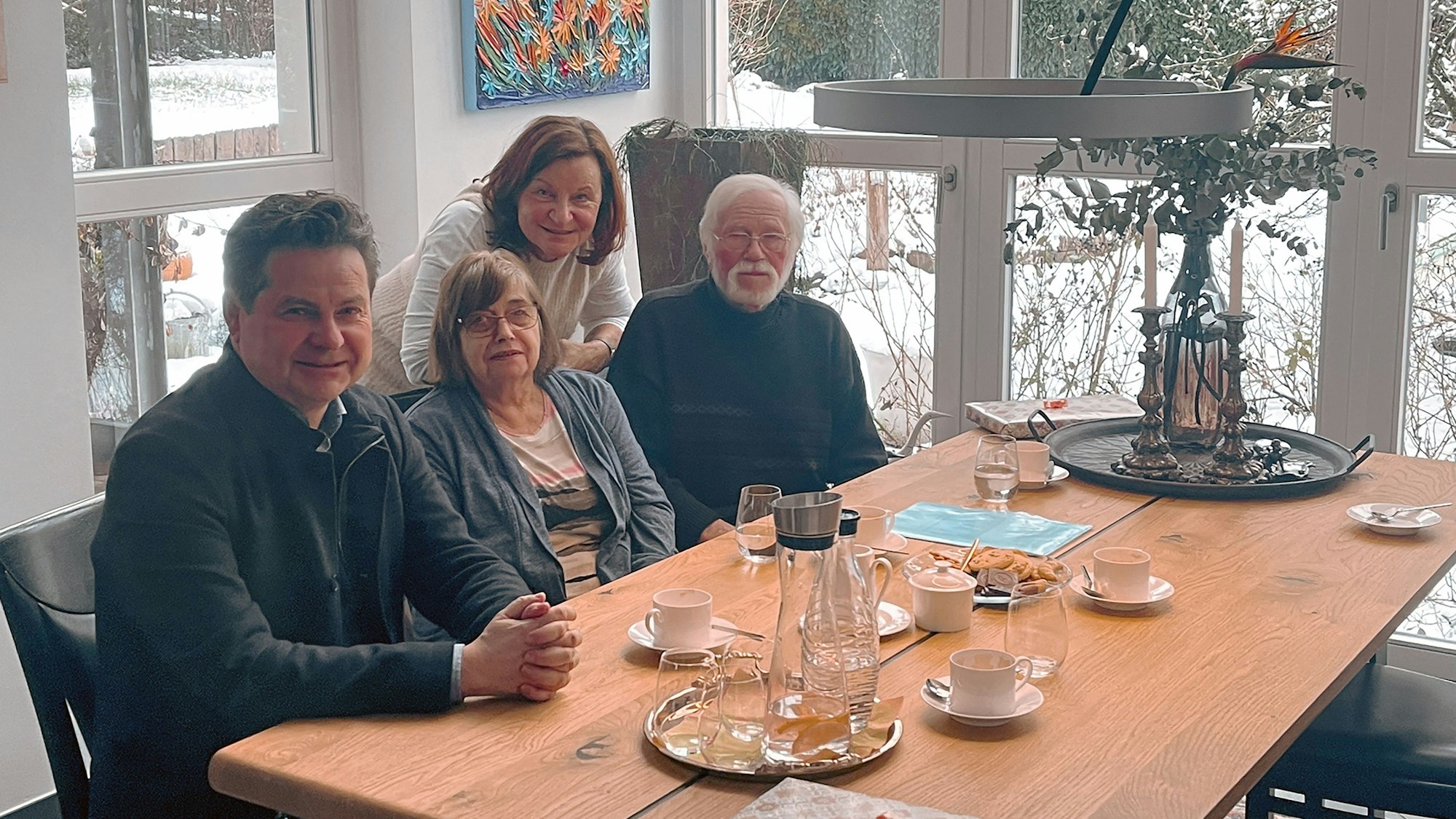 Vier Leute, zwei Frauen und zwei Männer, sitzen an einem großen Holztisch.