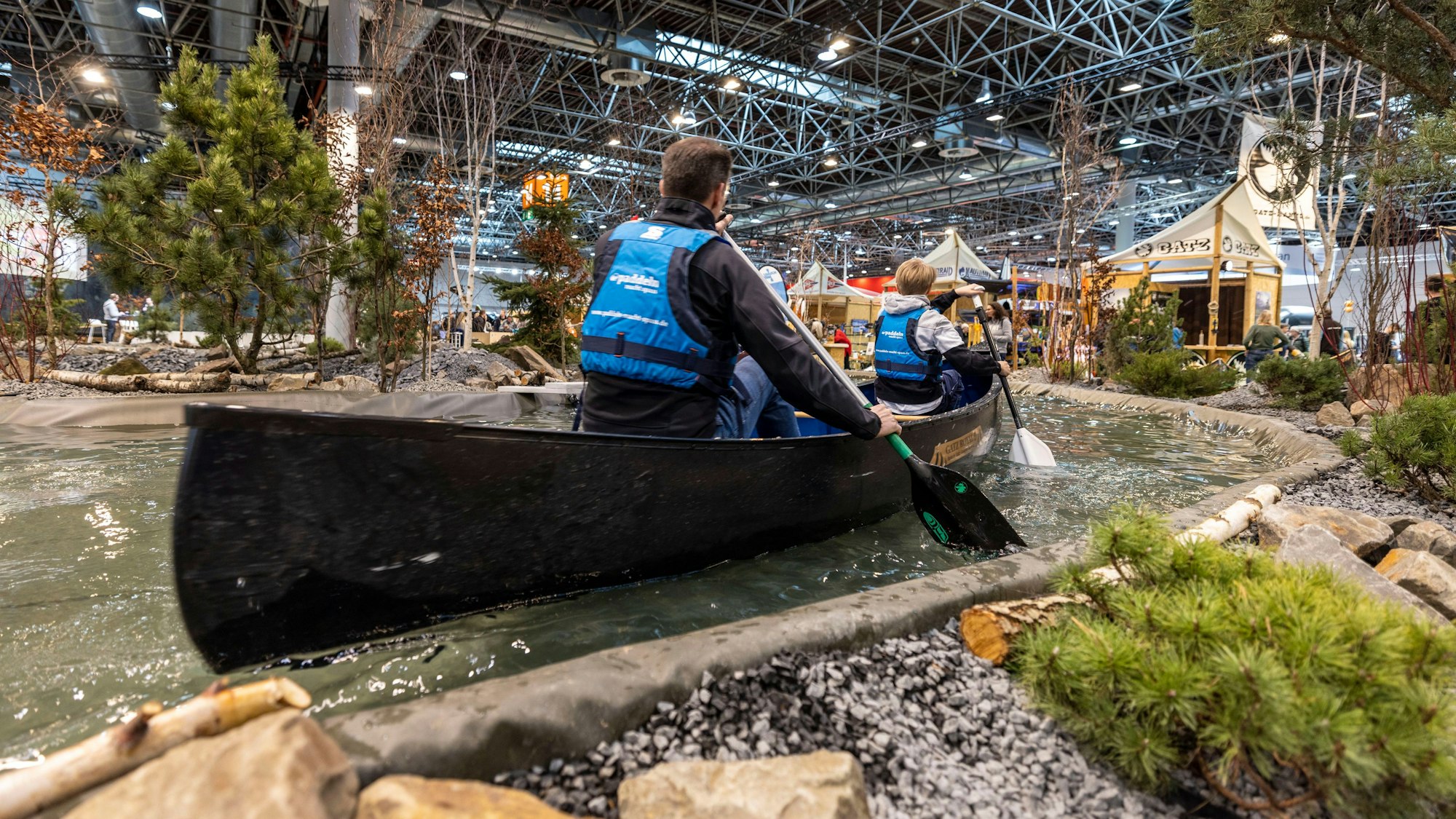 Messebesucher paddeln durch eine 100 Meter lange Kanu-Strecke, die in einer Messehalle zum Mitmachen einlädt.