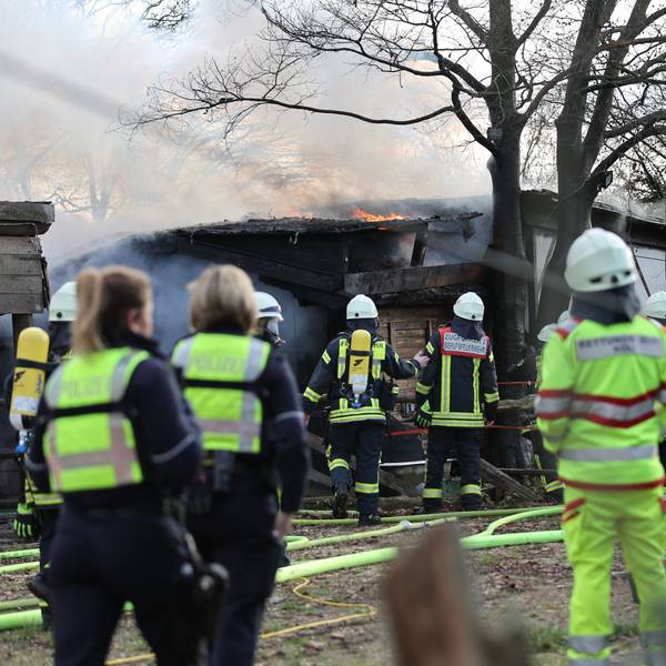 Feuerwehrleute, Sanitäter und Polizeibeamte stehen während eines Brands an einer Scheune im Kölner Stadtteil Rodenkirchen am Samstag, 29. Januar 2023. Bei dem Feuer ist eine Person tot aufgefunden worden.
