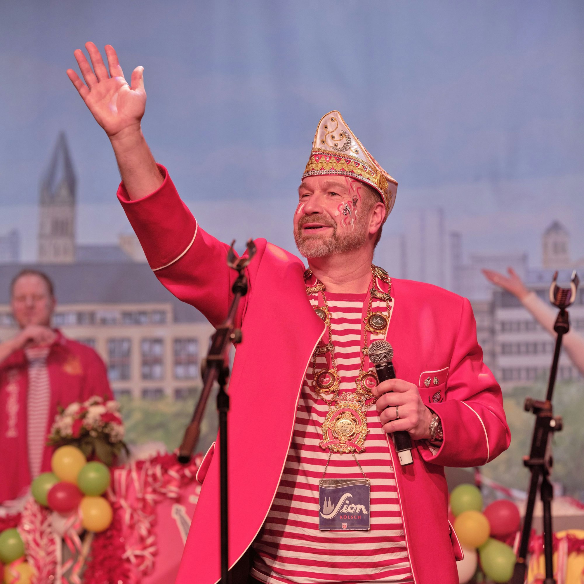 Der Sitzungspräsident Volker Weiniger steht im Saal und hebt die Hand zum Gruß.