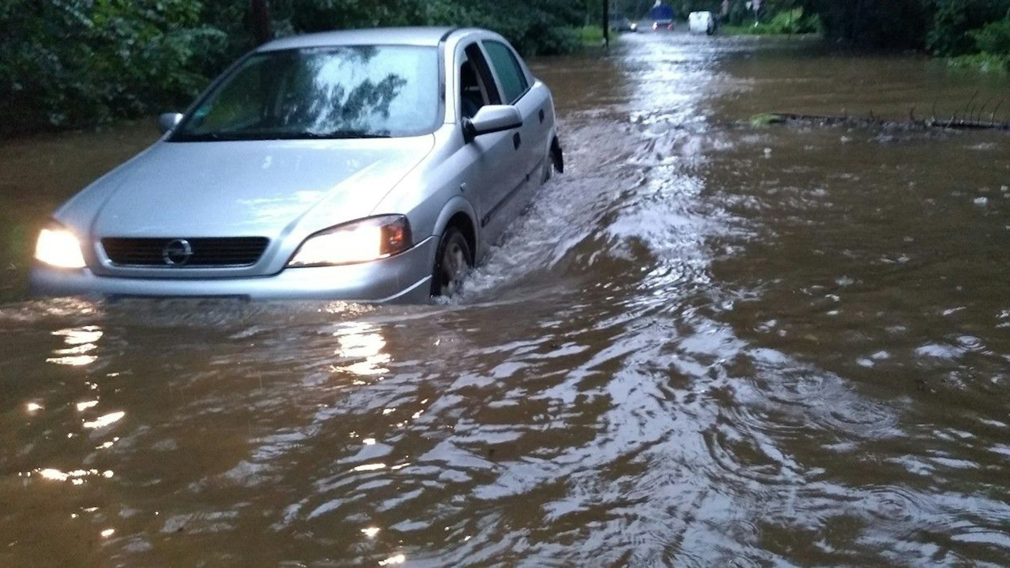 Ein Auto kämpft sich durch das hoch stehende Wasser auf dem Mauspfad in Köln-Dünnwald.