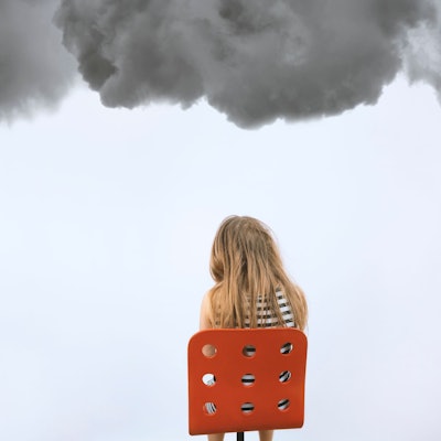 Ein Mädchen sitzt auf einem roten Stuhl unter dunklen Wolken.