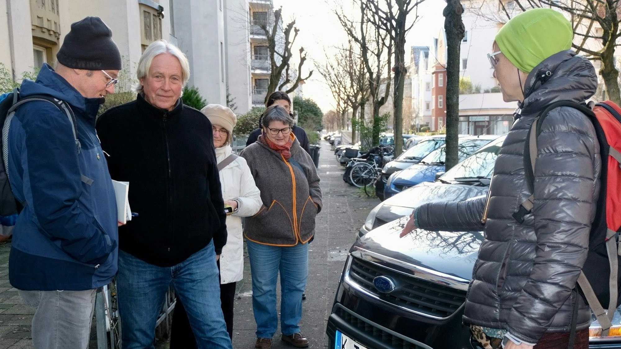 Die Anwohner stehen neben einem Auto, das den Gehweg zuparkt.