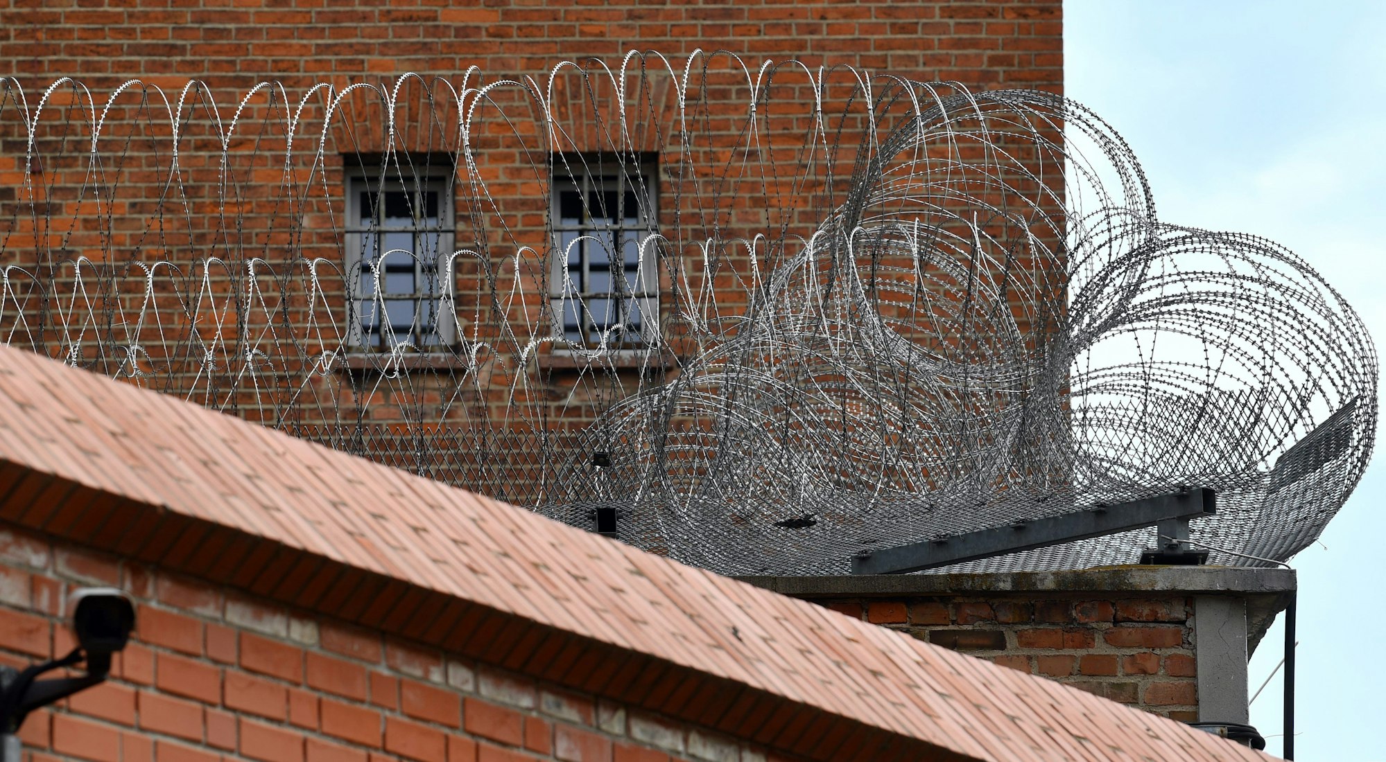 Blick auf die Justizvollzugsanstalt Halle/Saale. Backsteingebäude, im Vordergrund Stacheldraht.