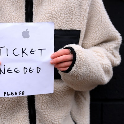 Eine Person hält einen Zettel in der Hand, auf den sie „Ticket needed – please“ geschrieben hat.