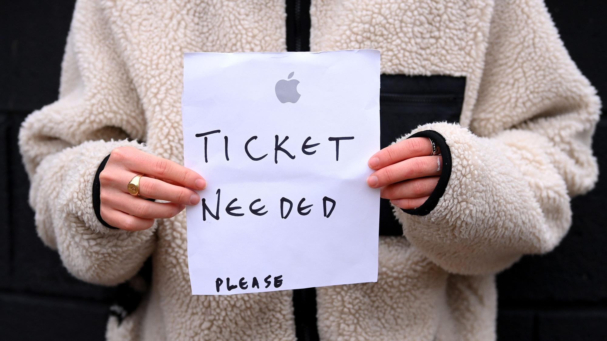 Eine Person hält einen Zettel in der Hand, auf den sie „Ticket needed – please“ geschrieben hat.