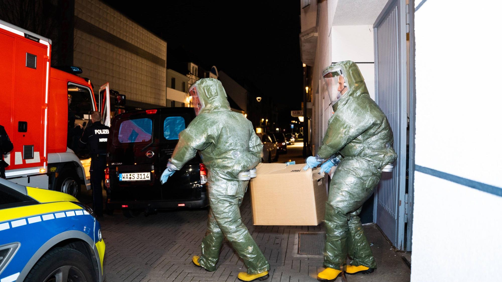 Männer in Schutzanzügen tragen einen Karton aus dem Haus, in dem ein Anti-Terror-Einsatz stattfand.