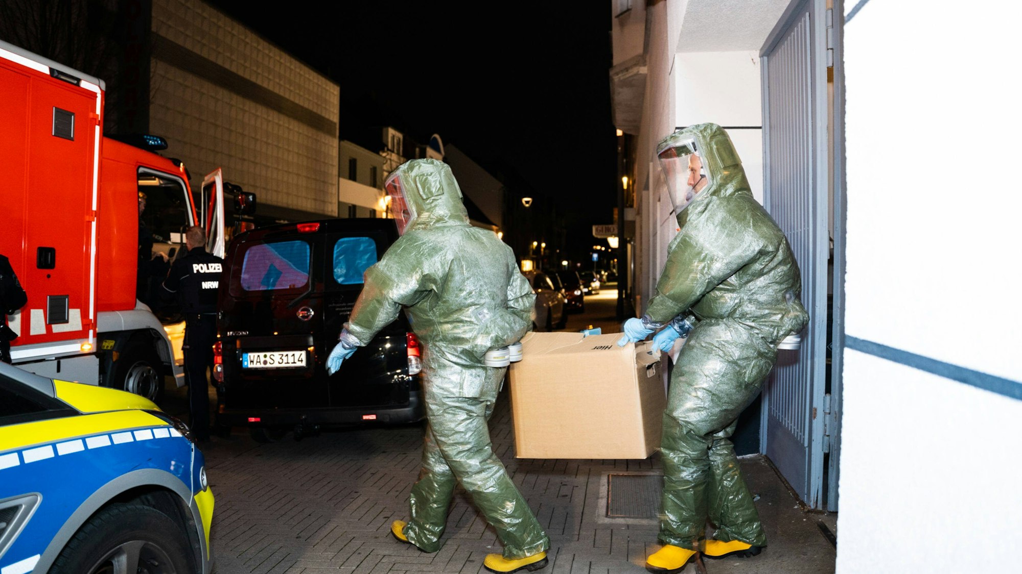 Männer in Schutzanzügen tragen einen Karton aus dem Haus, in dem ein Anti-Terror-Einsatz stattfand.
