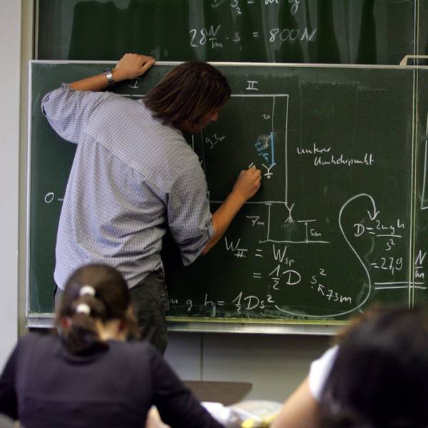 Ein Lehrer schreibt Physik-Formeln an die Tafel.