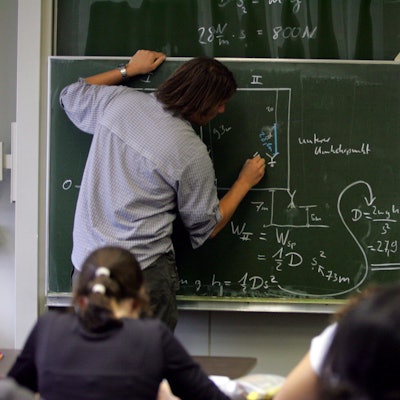 Ein Lehrer schreibt Physik-Formeln an die Tafel.
