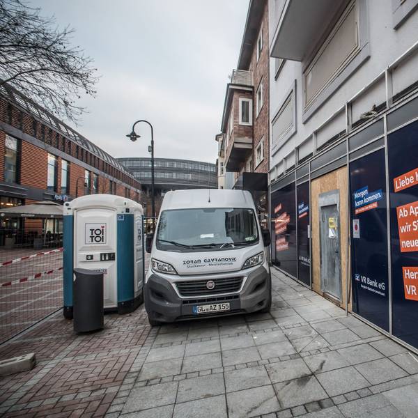 Vor einem Ladenlokal stehen ein Baufahrzeug und eine Baustellentoilette. An der Fassade wird angekündigt, dass in dem Ladenlokal die VR-Bank einzieht.