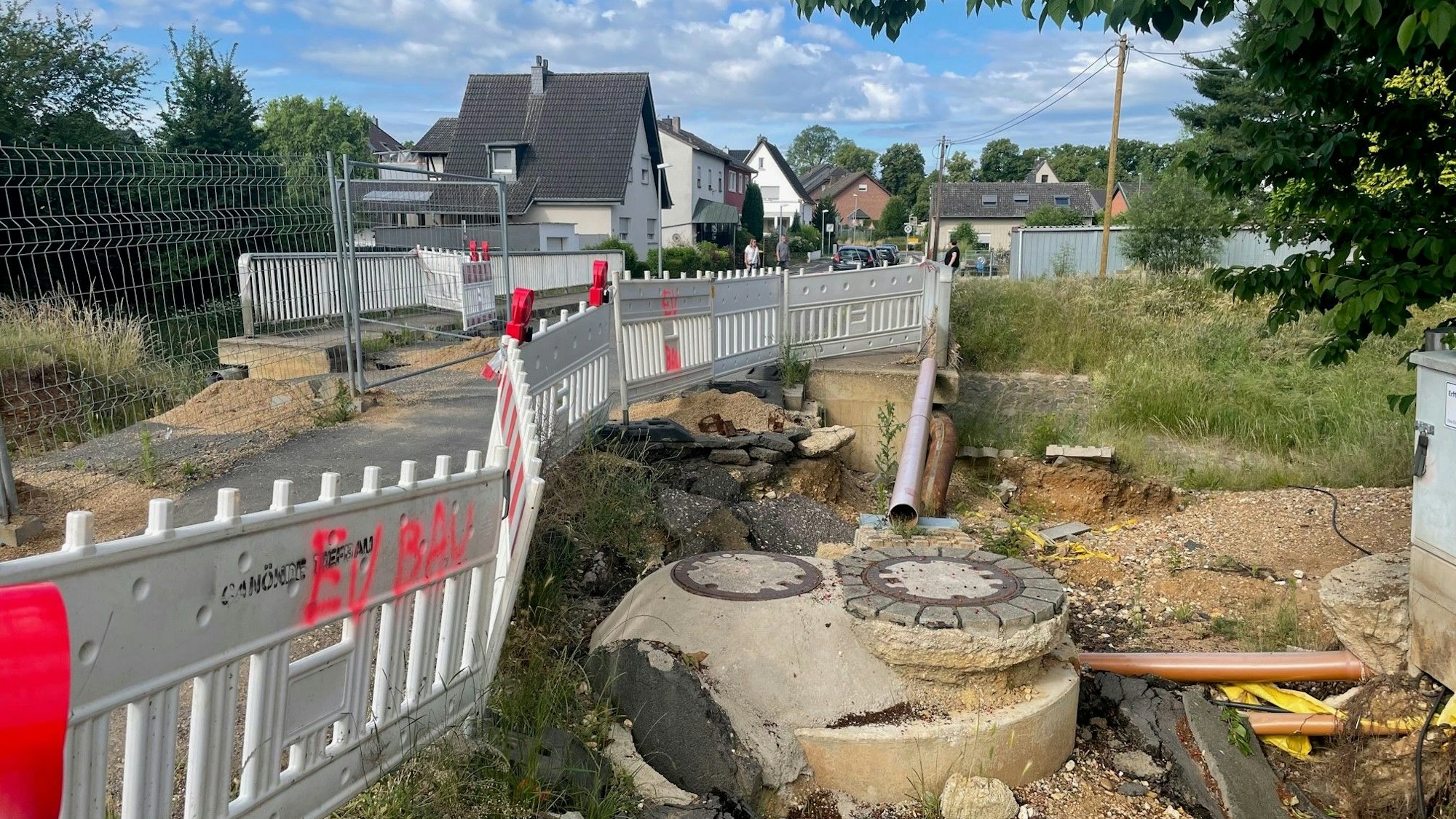 Eine von der Juli-Flut 2021 beschädigte Straße ist zu sehen, die teilweise immer noch abgesperrt ist, dahinter Wohnhäuser.