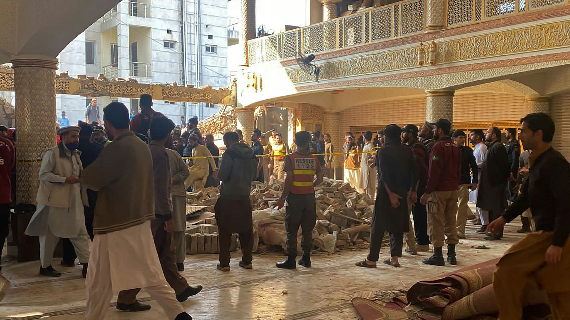 Personen und Sicherheitskräfte stehen nach der Explosion in Peshawar (Pakistan) an den Trümmern der Moschee. Die Explosion hat ein gewaltiges Loch in das Gebäude gerissen.