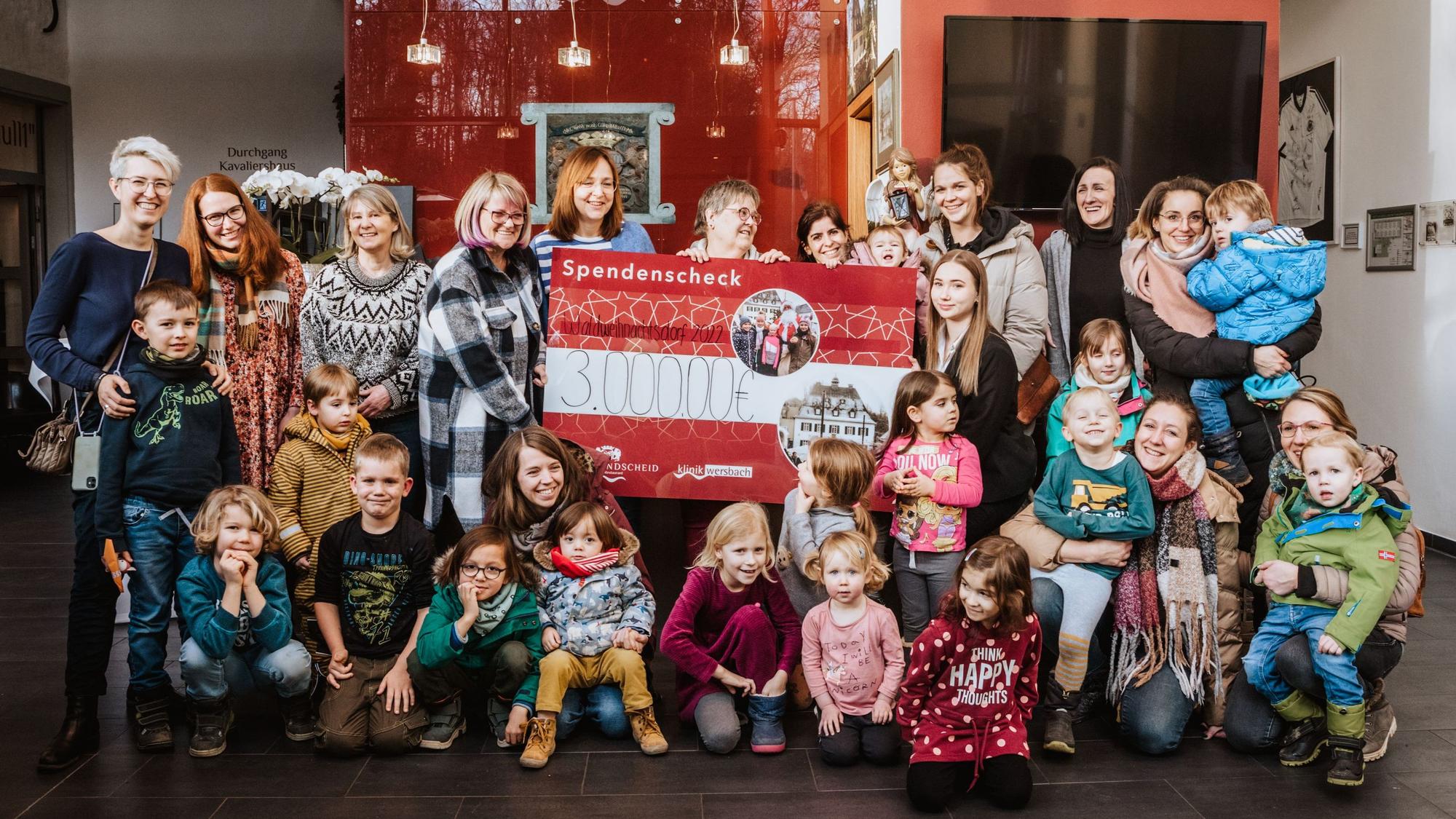 Yvonne und Marie-Celine Lammert halten einen Deko-Scheck über 3000 Euro, umgeben von Kindern und Erzieherinnen im Foyer von Gut Landscheid.
