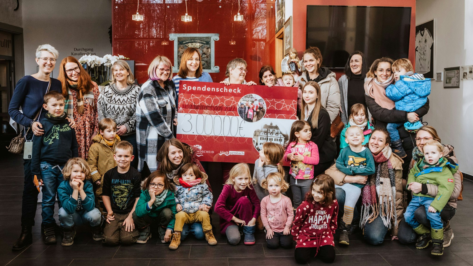 Yvonne und Marie-Celine Lammert halten einen Deko-Scheck über 3000 Euro, umgeben von Kindern und Erzieherinnen im Foyer von Gut Landscheid.