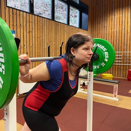Behinderte Kraftsportlerin Jessica Steinbrück drückt eine Langhantel mit grünen Gewichten in die Höhe.
