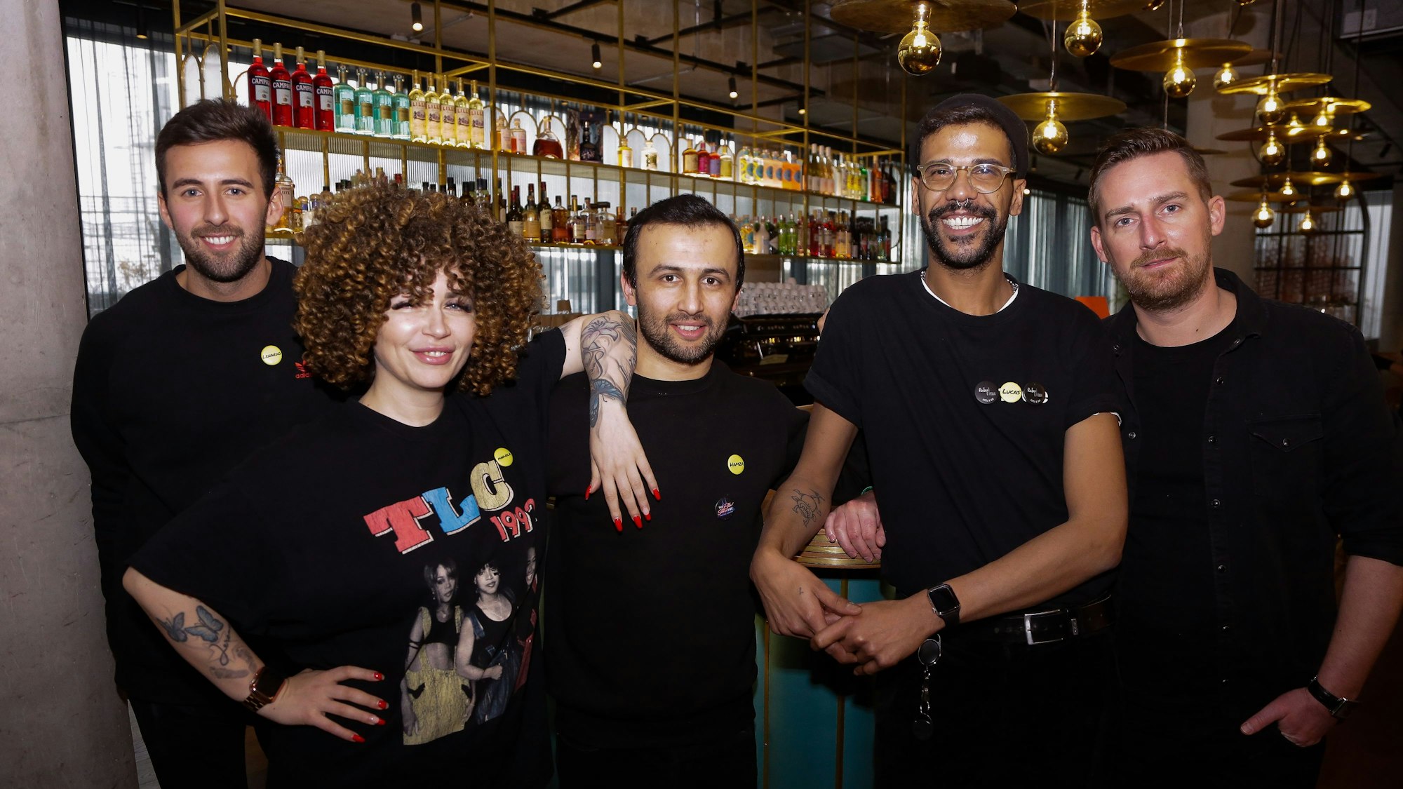 Der Hotelmanager Daniel Suré mit vier Mitarbeitern vor der Bar des Hotels. Eine Mitarbeiterin hat tätowierte Arme, ein Kollege ein Nasenpiercing und ebenfalls Tattoos.