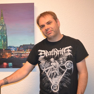 Gerald Bauer, Heavy-Metal-Blogger, vor einem Poster mit dem Kölner Dom.