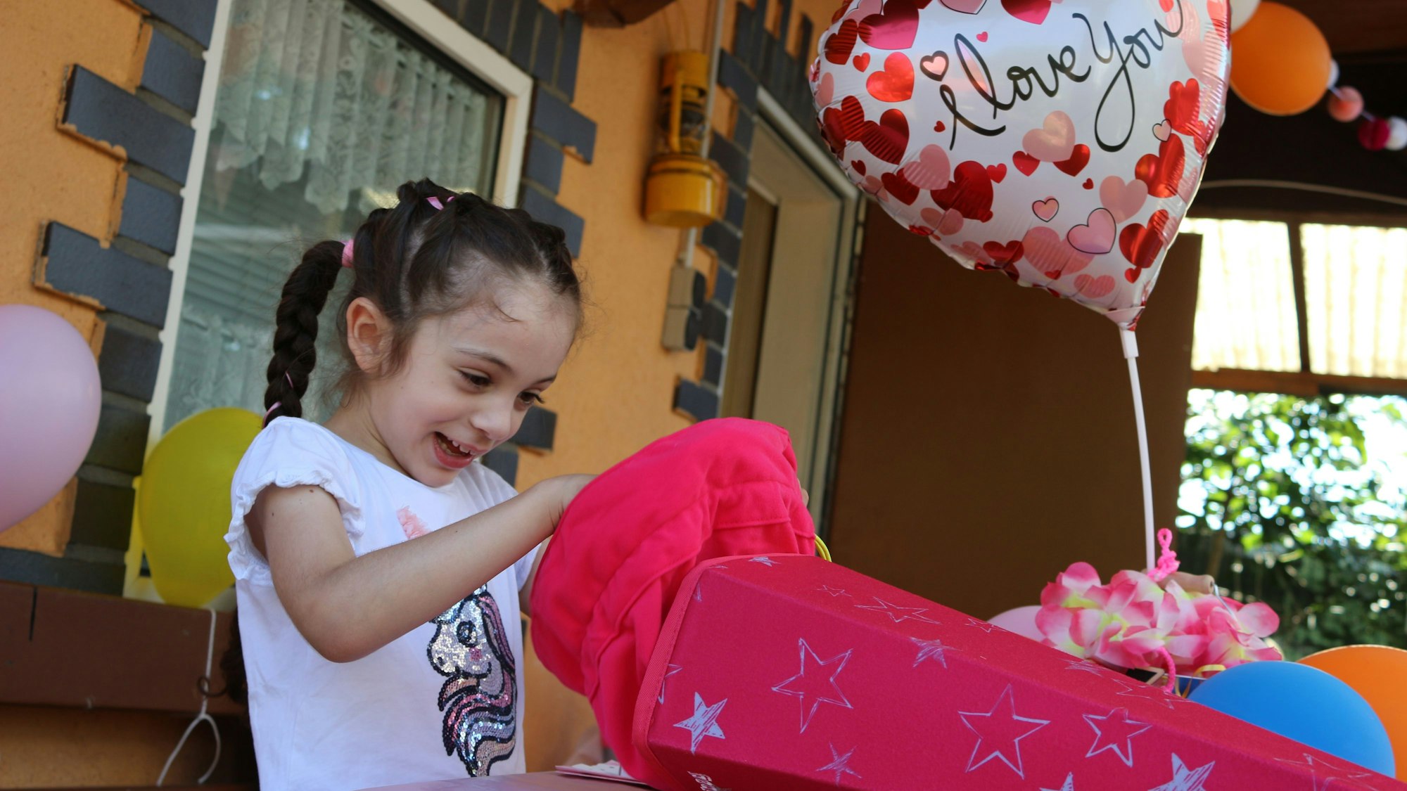 Sofia sitzt an einem bunt geschmückten Tisch und packt ihre pinkfarbene Schultüte aus.