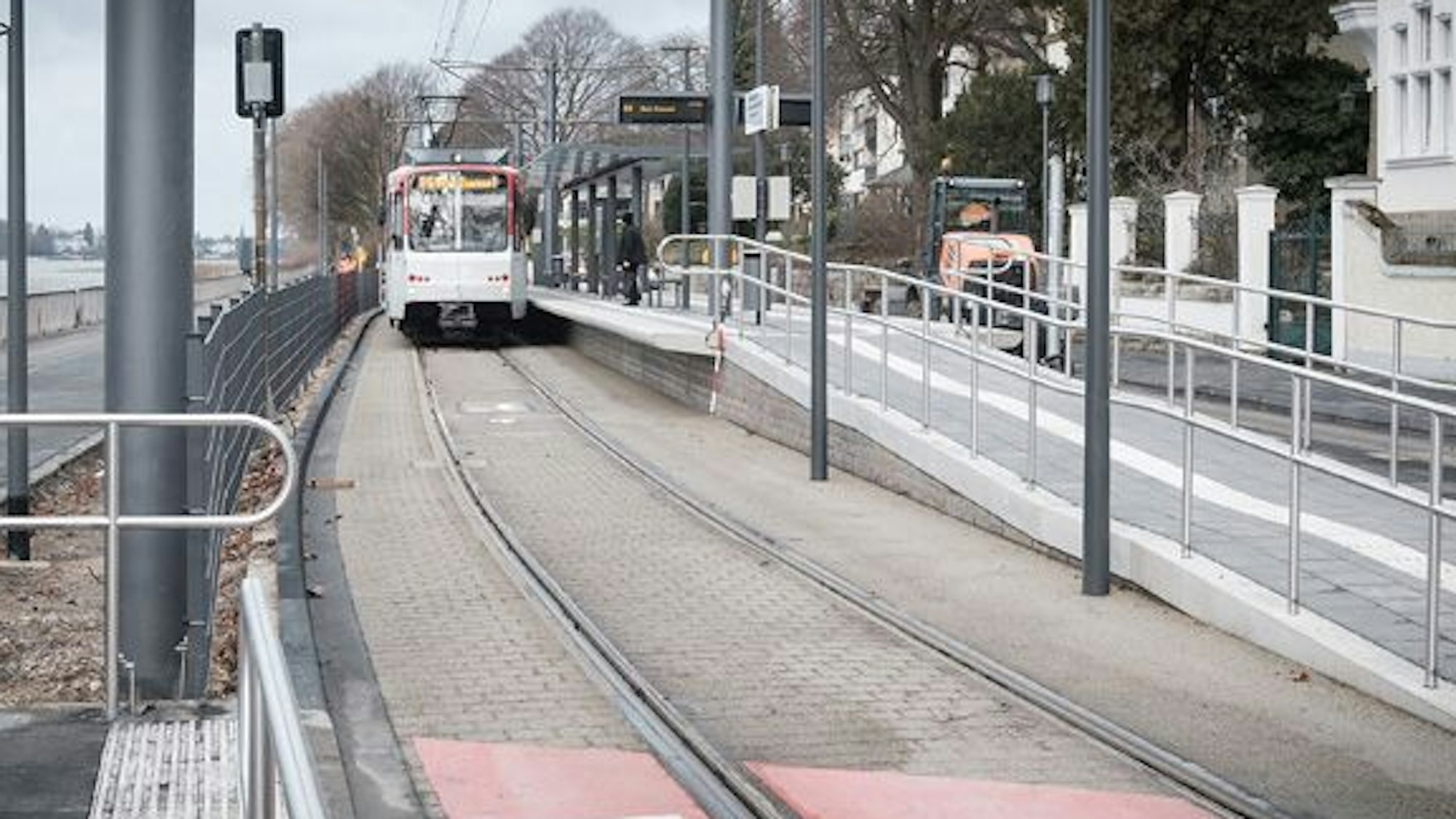 Eine rot-weiße Stadtbahn der Linie 66 steht am neuen Mittelbahnsteig Clemens-August-Straße in der Altstadt von Königswinter. Die Haltestelle hat einen Unterstand aus Glas und Stahl.