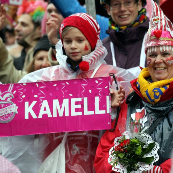08.02.2016: Rosenmontag in Köln: Jecke stehen verkleidet am Straßenrand und schauen auf den Rosenmontagszug. Ein Kind hält ein Schild, auf dem „Kamelle“ steht.