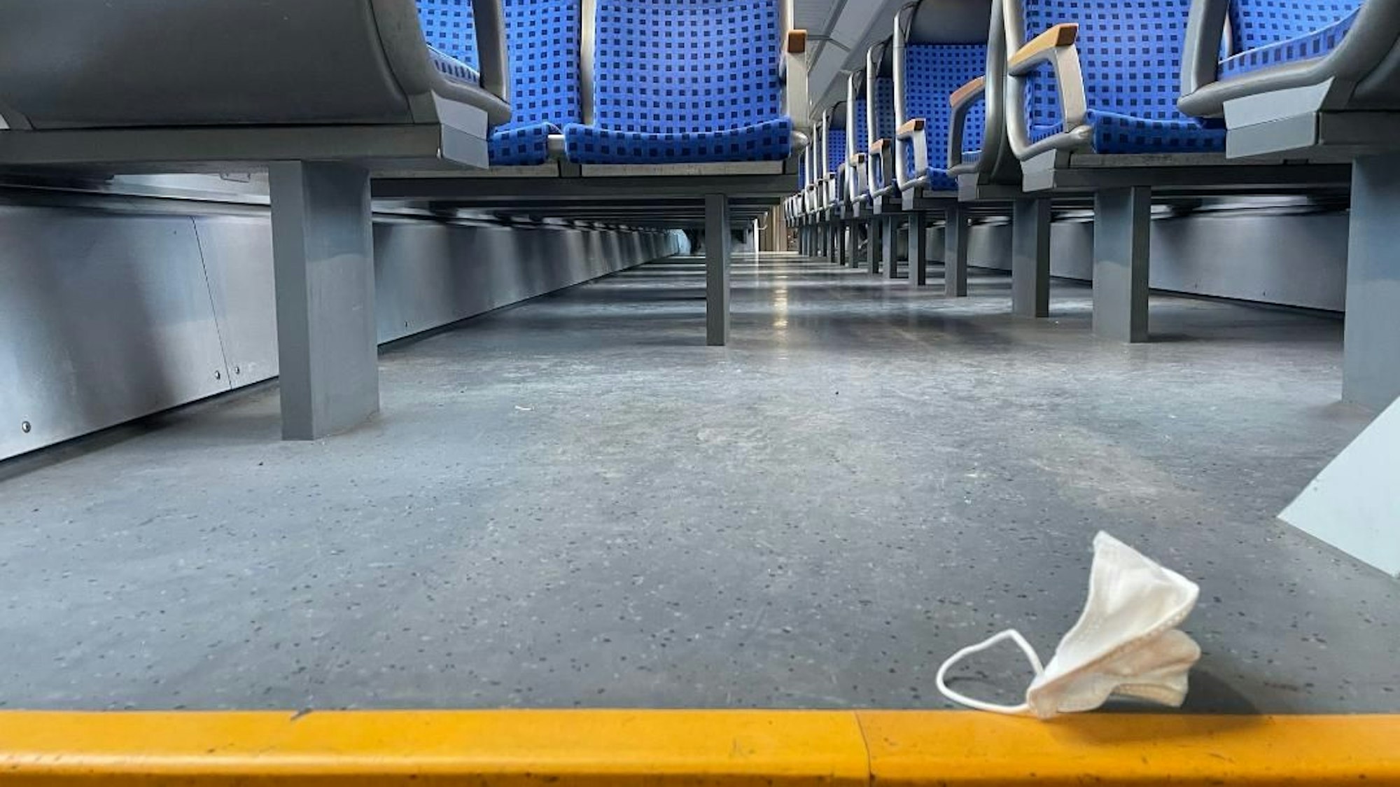 Eine Maske liegt in einem leeren Zugabteil.