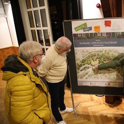 Zu sehen sind vier Menschen, die auf die großformatige Karte eines Spielplatzes schauen und über die Details sprechen.