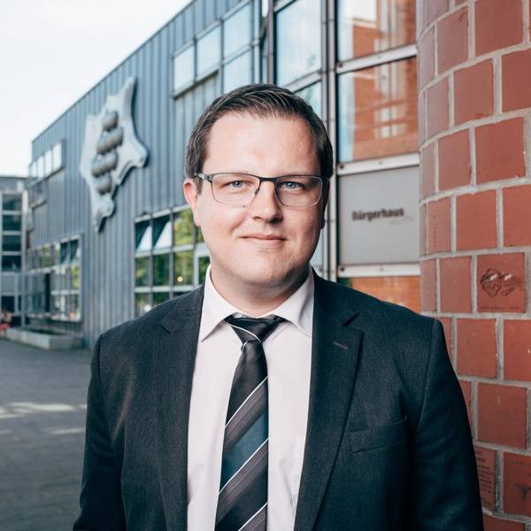 Matthias Neugebauer steht vor dem Stadthaus der Stadt Hürth. Er trägt Anzug und Brille.