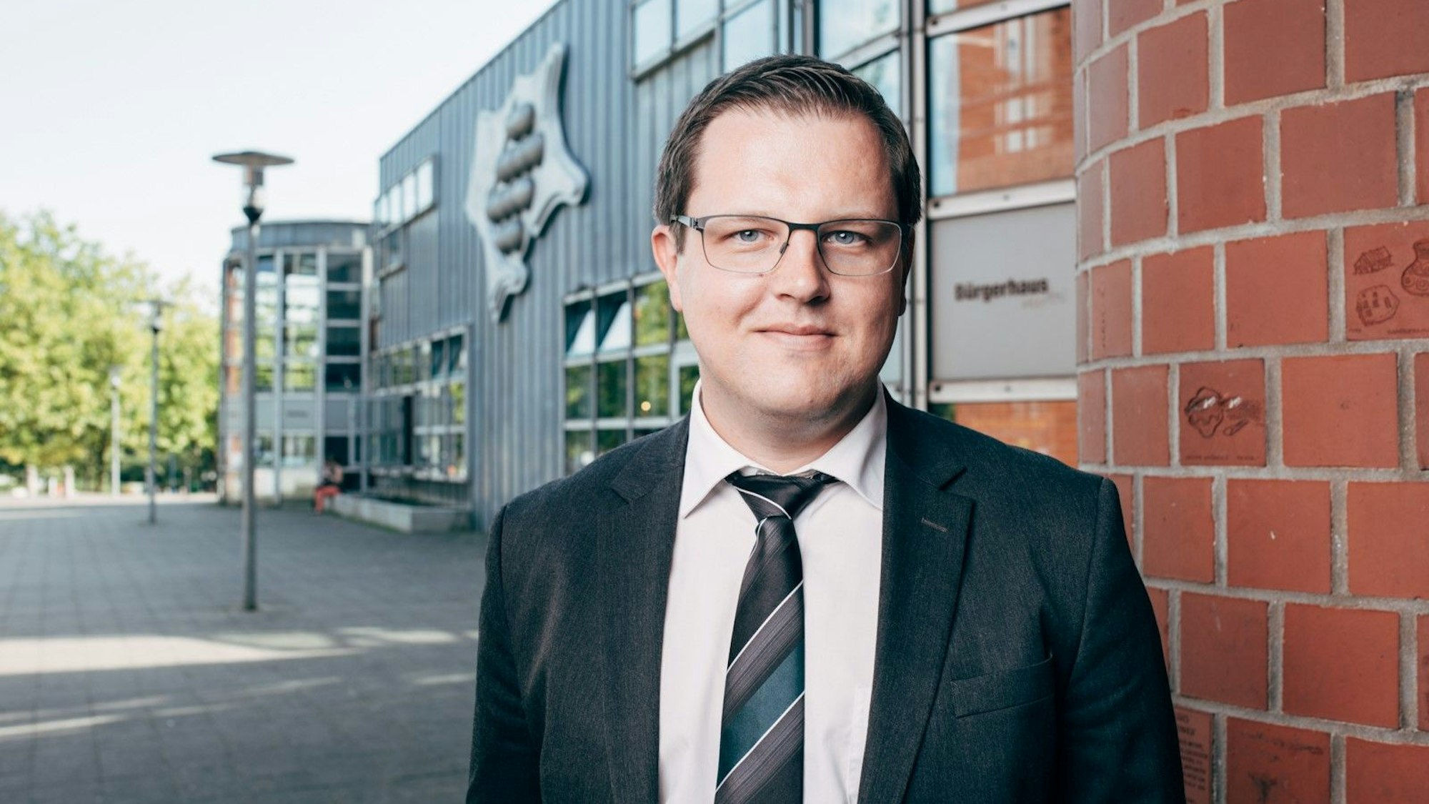 Matthias Neugebauer steht vor dem Stadthaus der Stadt Hürth. Er trägt Anzug und Brille.