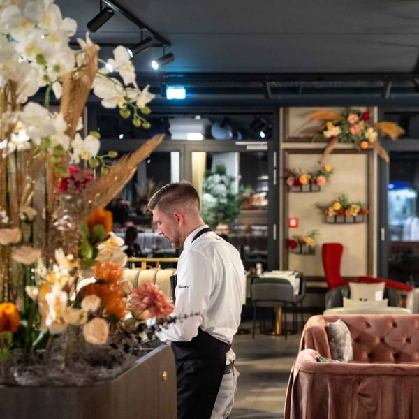 Das Bild zeigt ein Restaurant. Ein Kellner bedient an einem Tisch Gäste.
