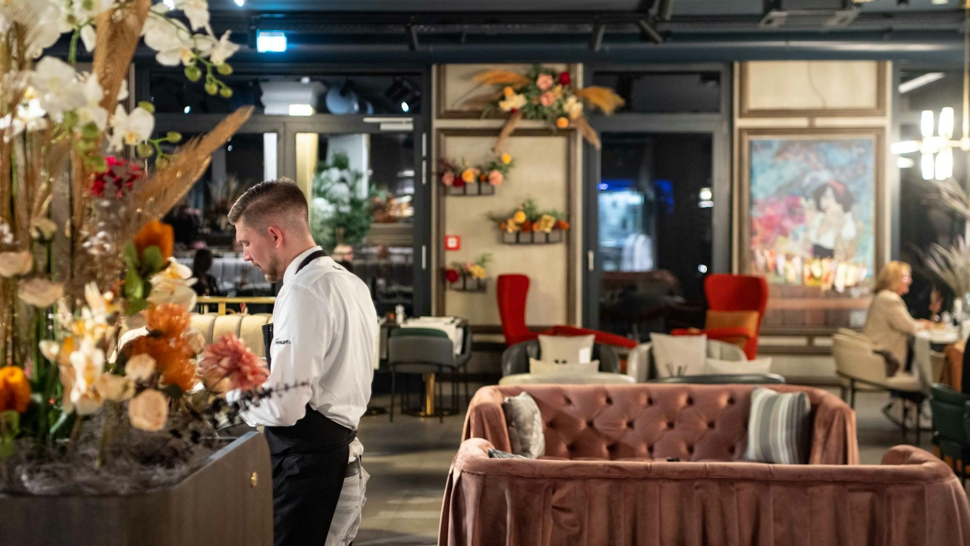 Ein Restaurant ist mit zahlreichen Blumen dekoriert, ein Kellner steht an einem Tisch.