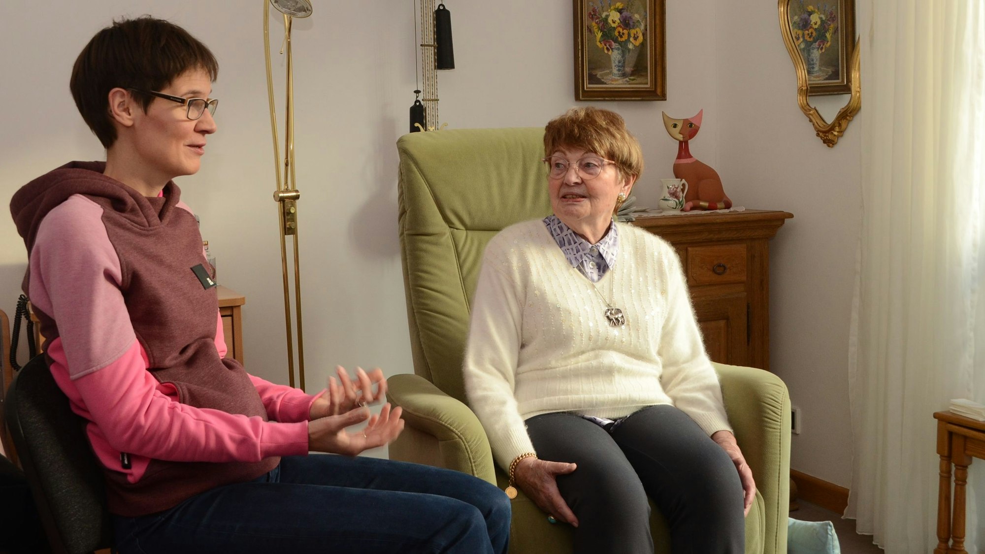Links sitzt Lena Judt, rechts Ingeborg Coenen. Die beiden reden miteinander. Sie sitzen in einem persönlich eingerichteten Raum.