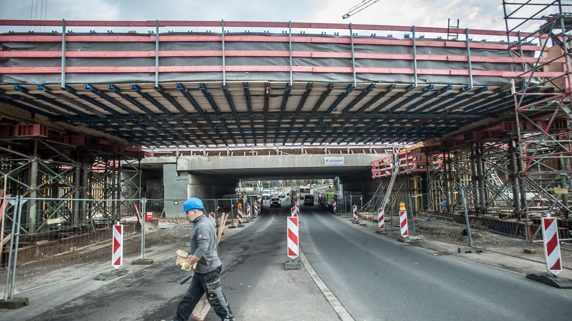Eine neu gebaute Brücke, die noch eine Baustelle ist, steht neben einer alten, ein Bauarbeiter mit blauem Schutzhelm geht entlang der Baustelle.