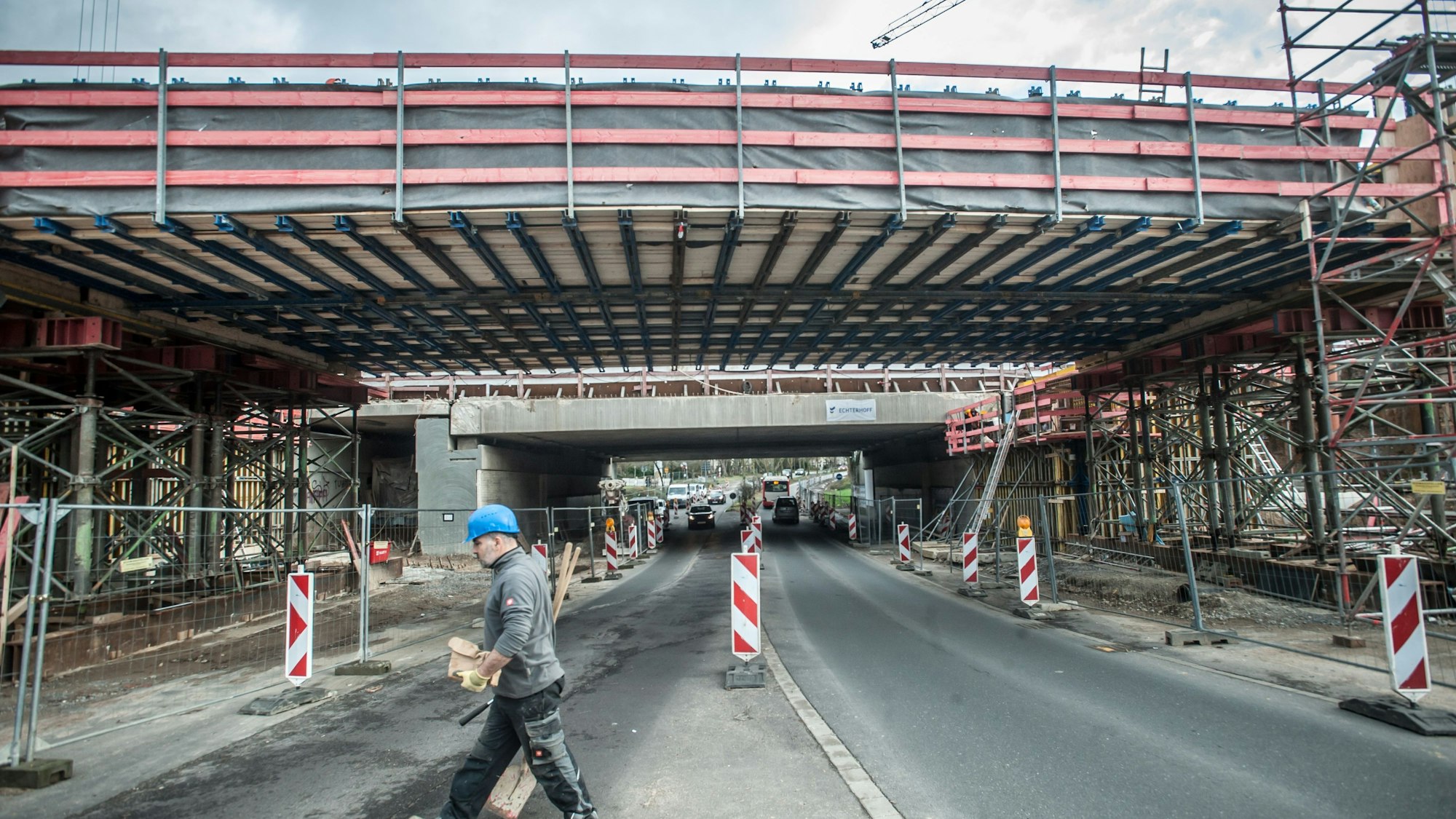 Eine neu gebaute Brücke, die noch eine Baustelle ist, steht neben einer alten, ein Bauarbeiter mit blauem Schutzhelm geht entlang der Baustelle.