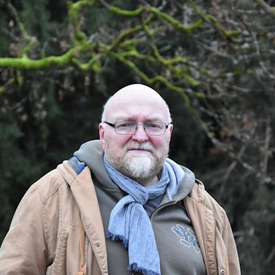 Man sieht Pedall vor einem Wald im Hintergrund stehen. Er schaut in die Kamera.