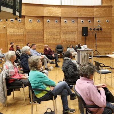 Menschen, die einem Vortrag anschauen, der von einer Leinwand begleitet wird.