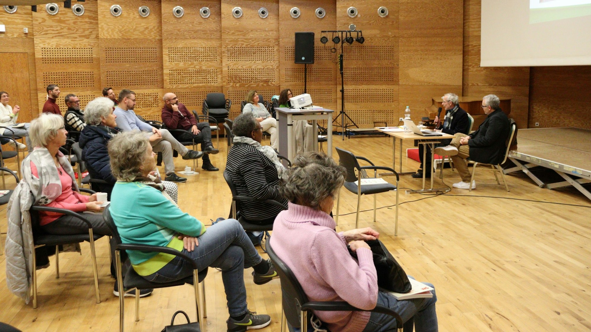 Menschen, die einem Vortrag anschauen, der von einer Leinwand begleitet wird.