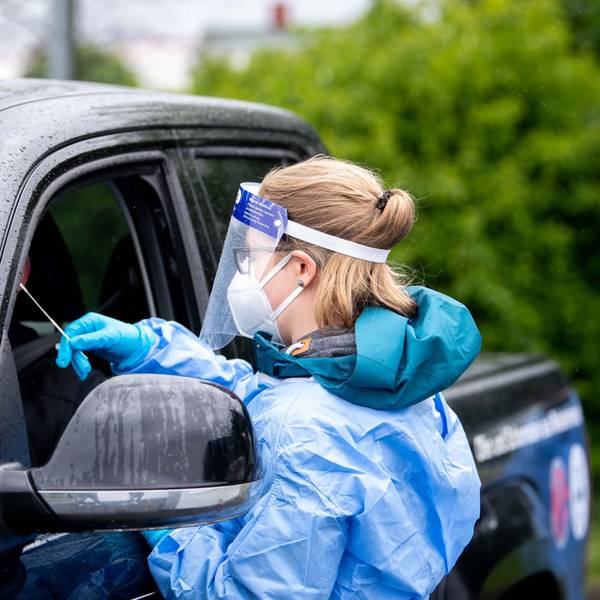 Eine Mitarbeiterin eines Corona-Testzentrums trägt Schutzkleidung und führt bei einem Autofahrer einen Test durch.