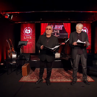 Alex Schneider (l.) und Victor Tabor stehen in schwarzen Anzügen auf einer Bühne.