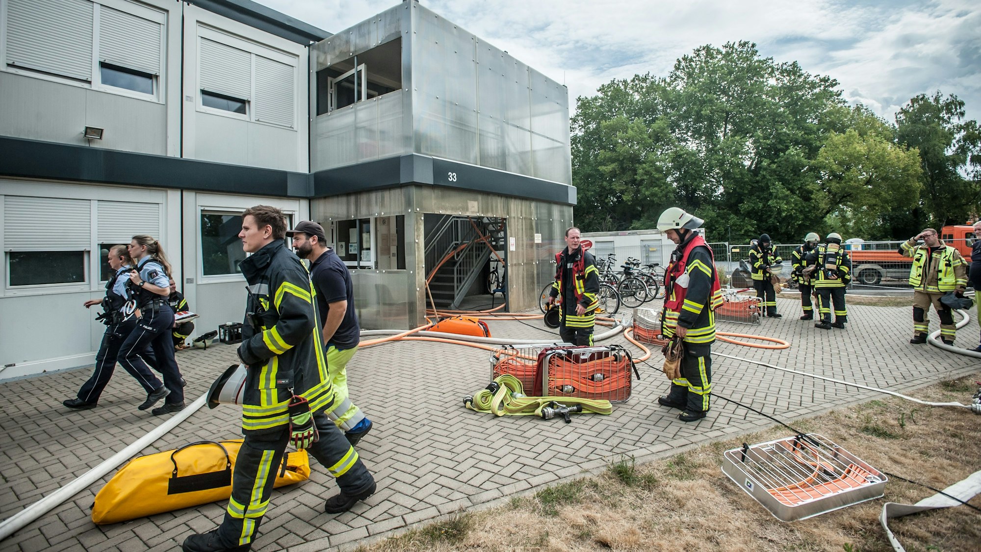 Feuerwehrleute stehen vor der Containersiedlung für Flüchtlinge in der Heinrich-Claes-Straße 33